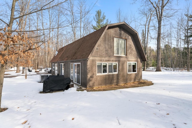 snow covered property featuring a gambrel roof and roof with shingles