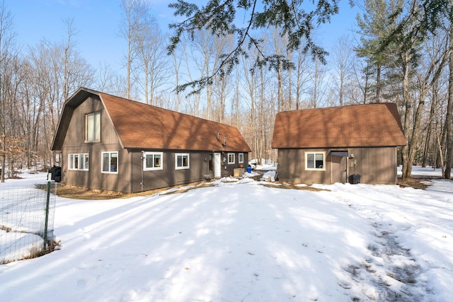 snow covered back of property with a barn, a gambrel roof, a shingled roof, and an outdoor structure