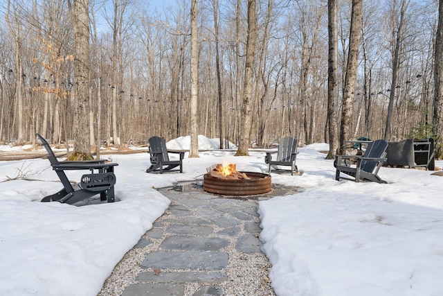 yard layered in snow with an outdoor fire pit and a forest view