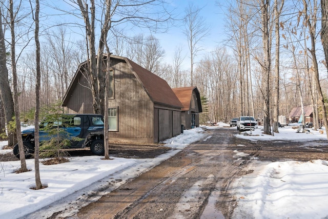 view of snowy exterior featuring a barn, a gambrel roof, and an outdoor structure