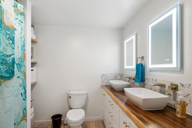 full bathroom featuring double vanity, toilet, baseboards, and a sink