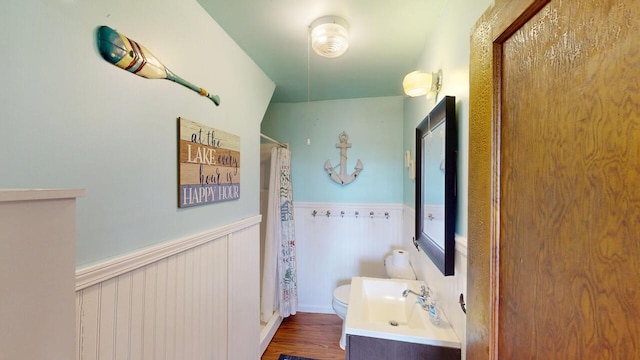 bathroom featuring a shower with curtain, toilet, wood finished floors, wainscoting, and vanity