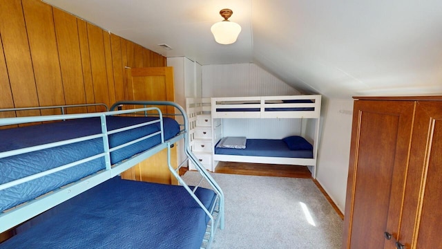 carpeted bedroom with wooden walls and vaulted ceiling