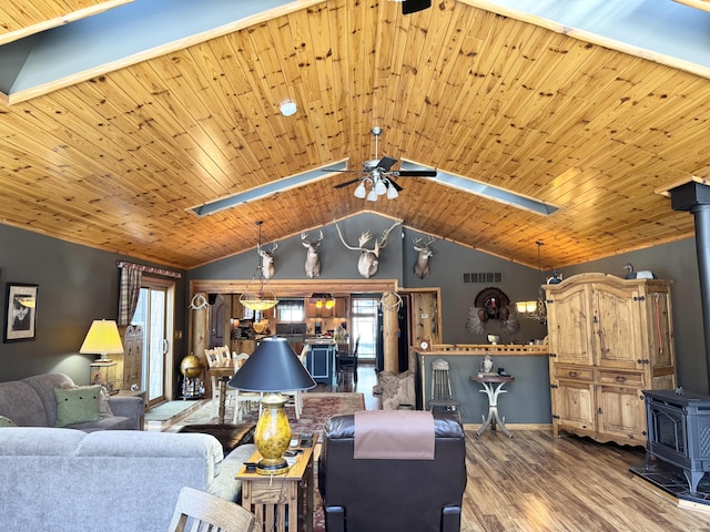 living area with visible vents, wood finished floors, baseboards, lofted ceiling, and a wood stove