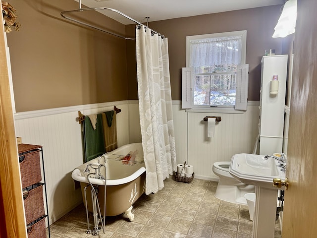 bathroom with a shower with curtain, a freestanding tub, toilet, and wainscoting