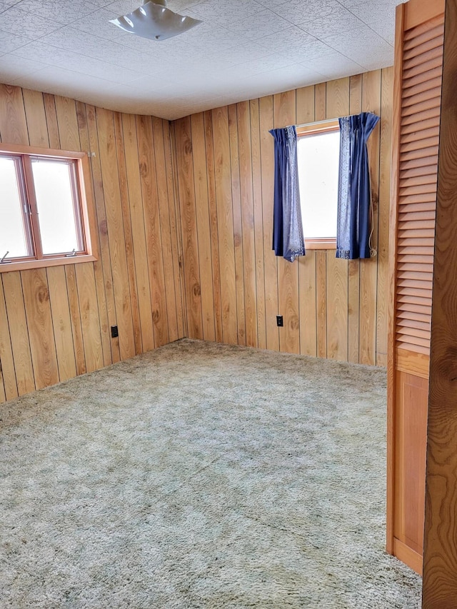 carpeted empty room featuring a textured ceiling and wood walls