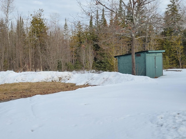 yard layered in snow with a view of trees, an outdoor structure, and a shed