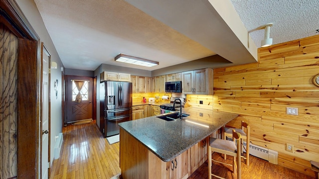 kitchen with a sink, appliances with stainless steel finishes, a peninsula, and light wood finished floors