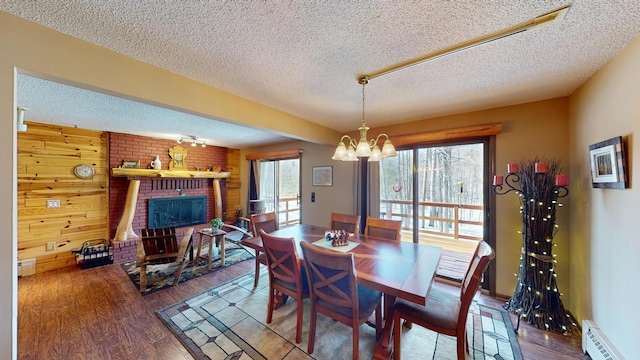 dining space featuring a brick fireplace, a baseboard heating unit, an inviting chandelier, wood finished floors, and a textured ceiling