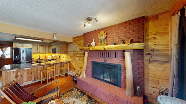 living area with a textured ceiling, wood finished floors, wood walls, baseboard heating, and a brick fireplace