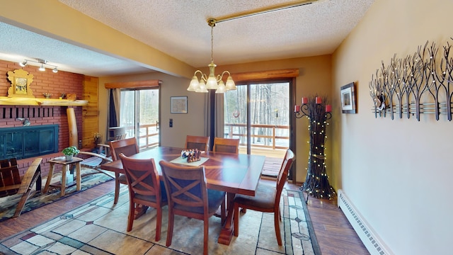 dining area with a notable chandelier, a textured ceiling, wood finished floors, baseboard heating, and a brick fireplace