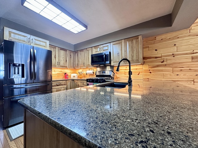 kitchen featuring wooden walls, dark stone counters, a peninsula, stainless steel appliances, and a sink