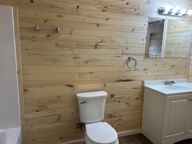 bathroom with toilet, wood walls, and vanity
