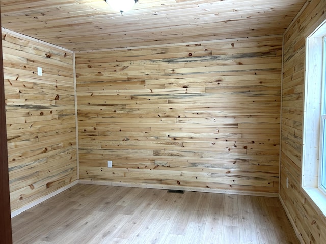 empty room with wooden walls, wood ceiling, and light wood-type flooring