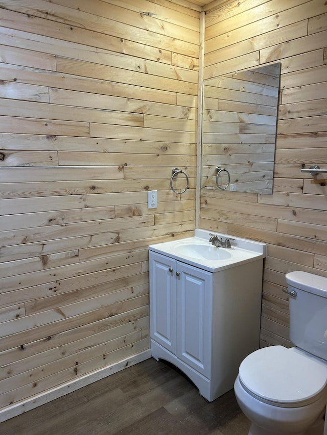 half bath featuring wood finished floors, toilet, wood walls, and vanity