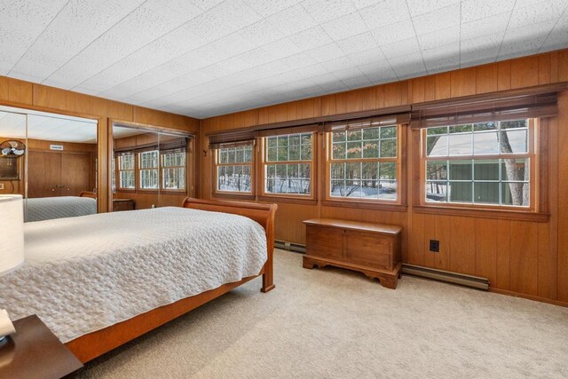 bedroom featuring wooden walls, multiple windows, a baseboard heating unit, and carpet floors