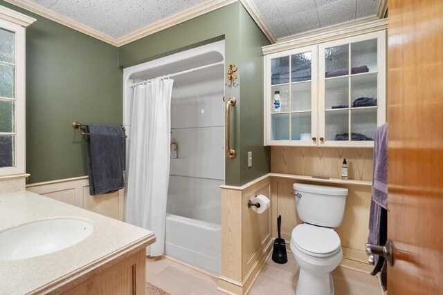 bathroom with a wainscoted wall, toilet, shower / bath combo, crown molding, and vanity