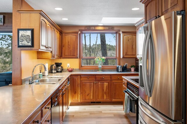 kitchen with light wood finished floors, a sink, black appliances, light countertops, and brown cabinets