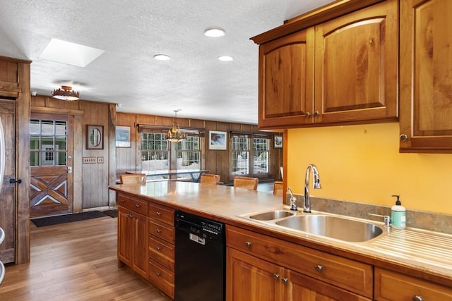 kitchen featuring light wood finished floors, dishwasher, brown cabinets, a skylight, and a sink