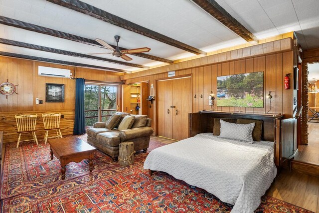 bedroom with beamed ceiling, a wall mounted AC, wooden walls, and wood finished floors