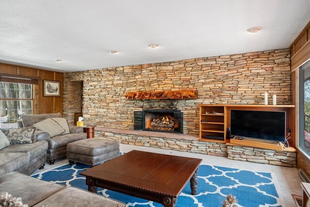 living area with a stone fireplace, wood walls, and carpet floors