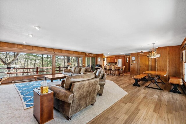 living area featuring light wood-style floors, wood walls, and a chandelier