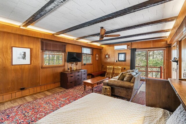 living room with beam ceiling, a healthy amount of sunlight, a wall unit AC, and wood finished floors