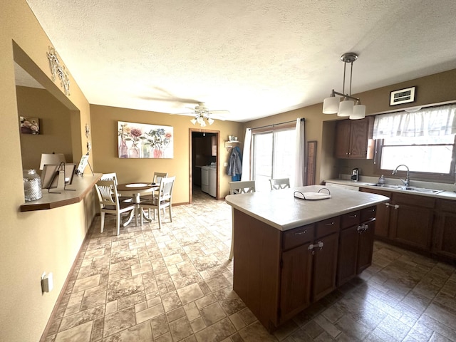 kitchen featuring a ceiling fan, a sink, a center island, dark brown cabinetry, and light countertops