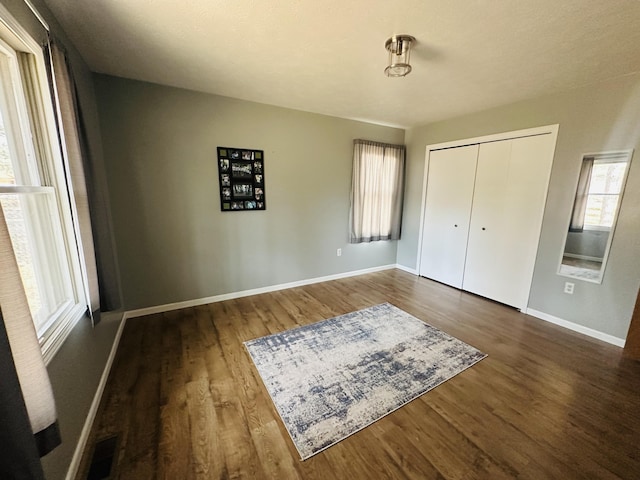 unfurnished bedroom featuring visible vents, wood finished floors, baseboards, and a closet