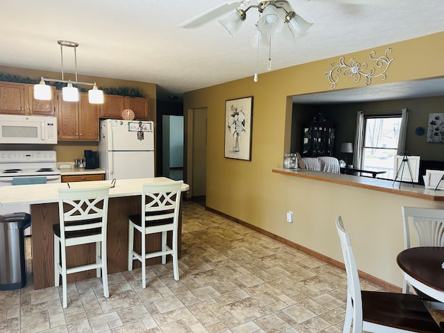 kitchen with baseboards, white appliances, a breakfast bar area, and light countertops