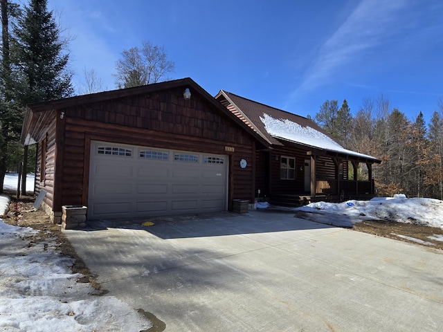 cabin featuring covered porch, driveway, an attached garage, and log veneer siding