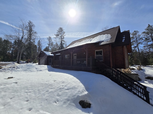 snow covered property featuring a porch, faux log siding, stairway, an outdoor structure, and an attached garage