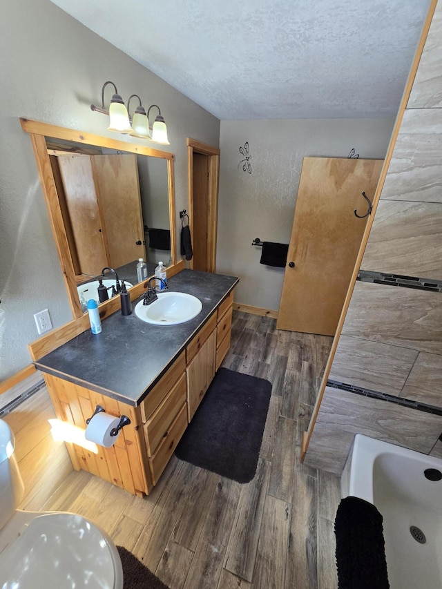 bathroom with vanity, wood finished floors, a bathing tub, baseboards, and a textured ceiling