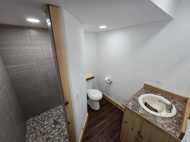 bathroom with baseboards, toilet, a tile shower, wood finished floors, and vanity