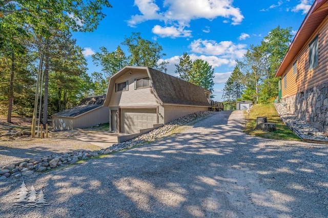 6122 Beach Rd, Johannesburg, MI 49751 - view of home's exterior featuring an attached garage, a gambrel roof, driveway, an outbuilding, and a shingled roof