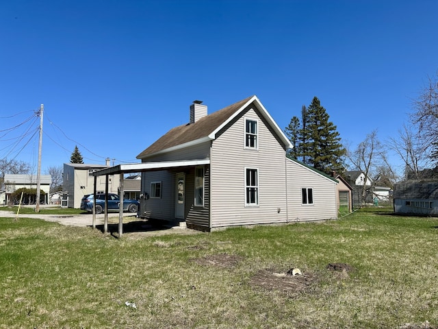 1117 Mackinaw Ave, Cheboygan, MI 49721 - back of property featuring a lawn, a chimney, an attached carport, and driveway