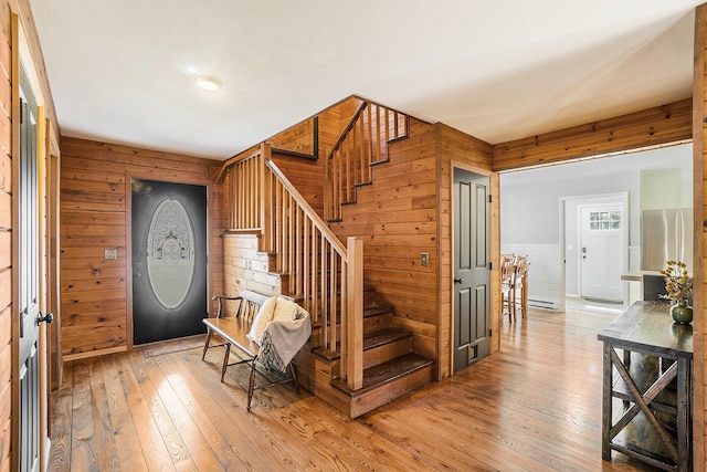 foyer entrance featuring light wood-type flooring, wood walls, stairs, and a wainscoted wall