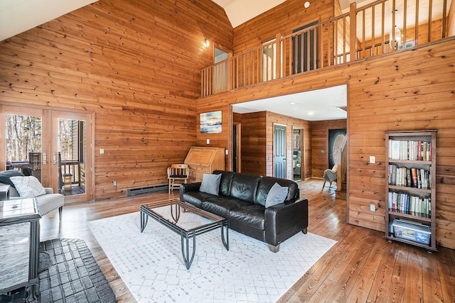 living area with french doors, a high ceiling, wooden walls, and wood-type flooring