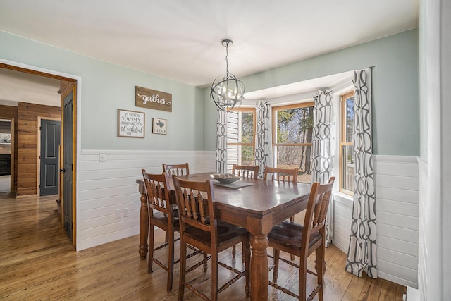 dining room featuring wainscoting, light wood finished floors, a chandelier, and wooden walls