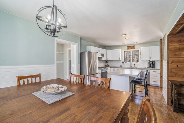 dining area featuring a notable chandelier, a wainscoted wall, and dark wood-type flooring