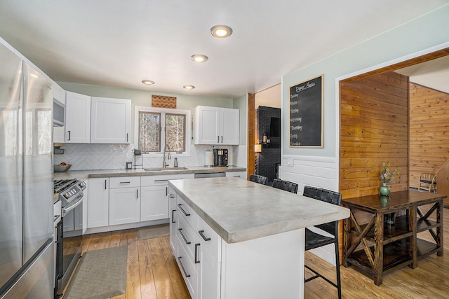 kitchen featuring light wood finished floors, stainless steel appliances, decorative backsplash, a breakfast bar area, and white cabinetry