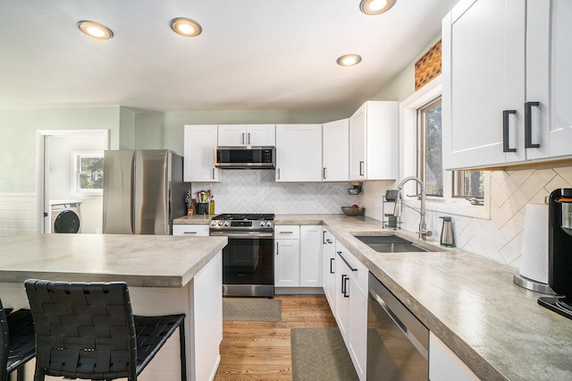 kitchen featuring white cabinets, a sink, appliances with stainless steel finishes, washer / clothes dryer, and a breakfast bar area