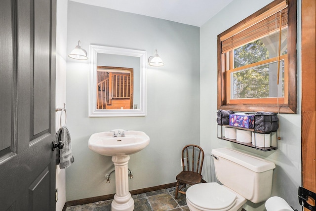bathroom featuring toilet, baseboards, and stone tile floors