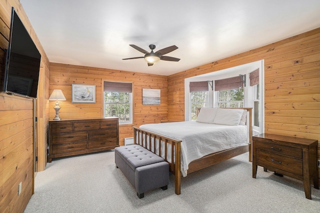 bedroom featuring multiple windows, wood walls, a ceiling fan, and light carpet