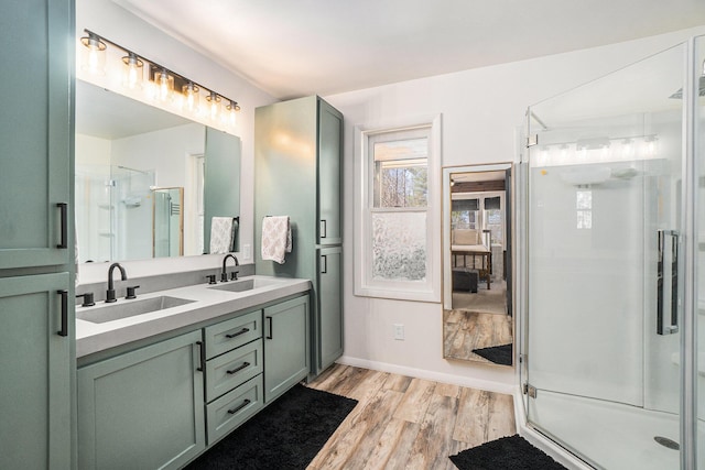 bathroom featuring double vanity, a shower stall, wood finished floors, and a sink