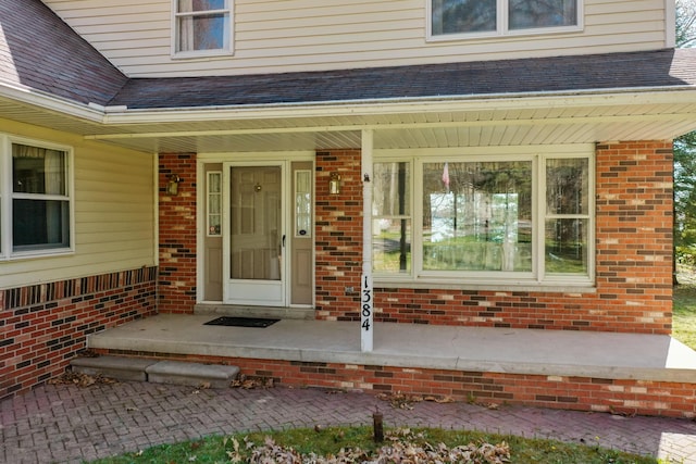 1384 W Higgins Lake Dr, Roscommon, MI 48653 - view of exterior entry featuring a porch, brick siding, and roof with shingles