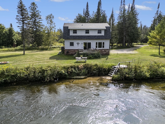back of property with a water view, roof with shingles, and a yard