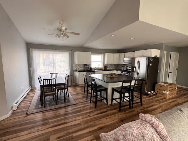 dining space with a baseboard heating unit, vaulted ceiling, recessed lighting, dark wood finished floors, and ceiling fan