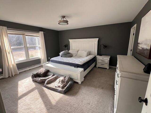bedroom with a baseboard heating unit, light colored carpet, and baseboards