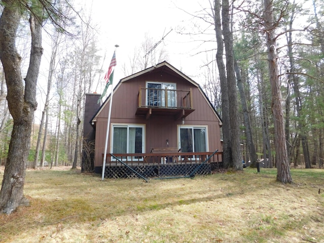 view of front facade with a wooden deck, a chimney, a front yard, and a balcony